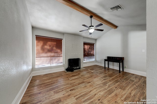 unfurnished living room with a wood stove, ceiling fan, light hardwood / wood-style flooring, and lofted ceiling with beams