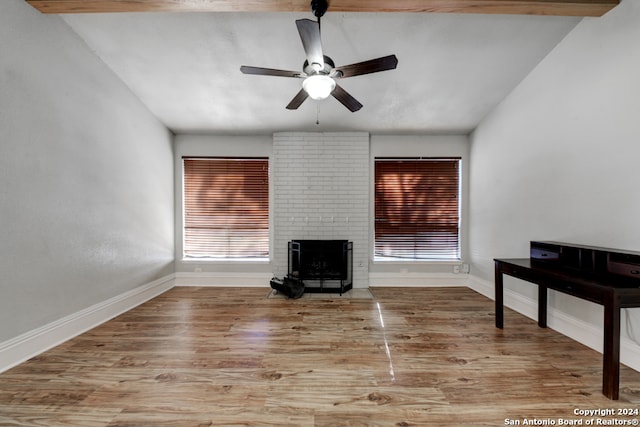 living room with a wood stove, ceiling fan, lofted ceiling with beams, and light wood-type flooring