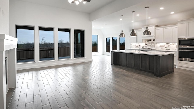 kitchen featuring white cabinetry, stainless steel appliances, an island with sink, decorative backsplash, and decorative light fixtures