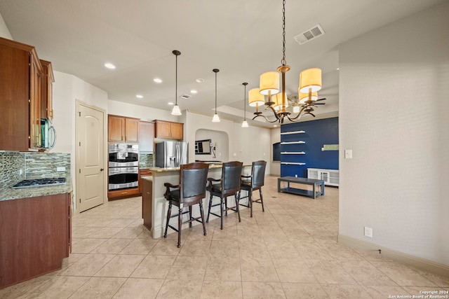 kitchen with stainless steel appliances, an inviting chandelier, tasteful backsplash, pendant lighting, and a center island with sink