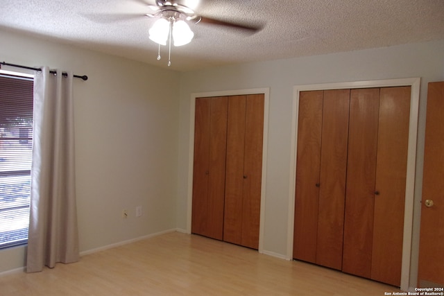 unfurnished bedroom featuring two closets, a textured ceiling, light hardwood / wood-style floors, and ceiling fan