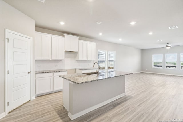 kitchen with light stone countertops, sink, a center island with sink, light hardwood / wood-style flooring, and white cabinets