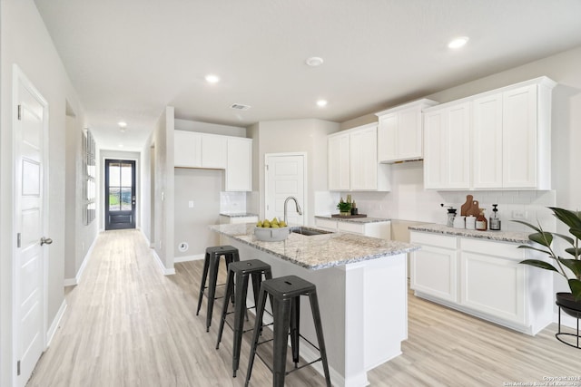 kitchen with a center island with sink, white cabinets, and light wood-type flooring