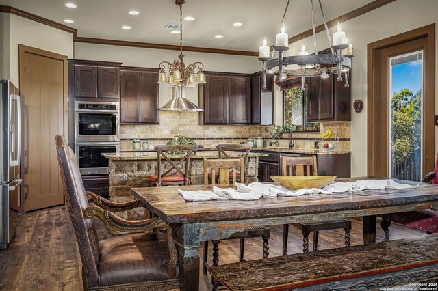 kitchen featuring pendant lighting, light stone counters, appliances with stainless steel finishes, dark hardwood / wood-style flooring, and dark brown cabinetry