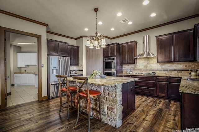 kitchen with hanging light fixtures, wall chimney exhaust hood, a kitchen island, dark hardwood / wood-style flooring, and stainless steel appliances