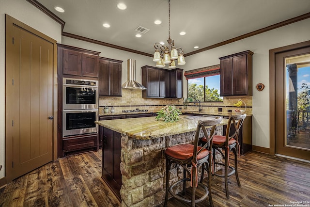 kitchen featuring light stone countertops, a center island, wall chimney exhaust hood, dark wood-type flooring, and appliances with stainless steel finishes