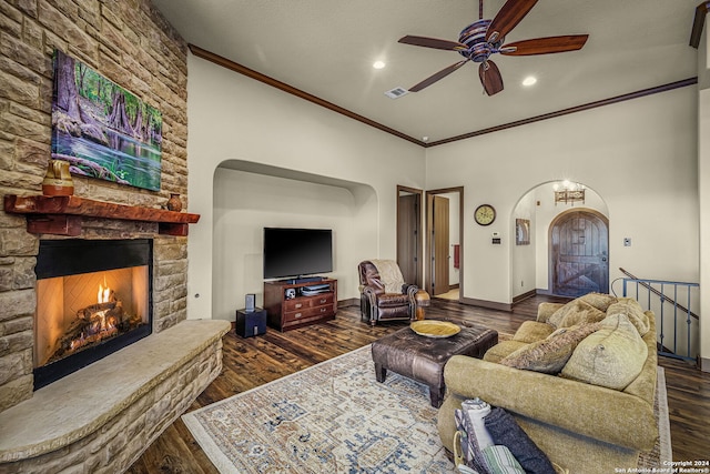 living room with ceiling fan, dark wood-type flooring, a stone fireplace, a textured ceiling, and ornamental molding