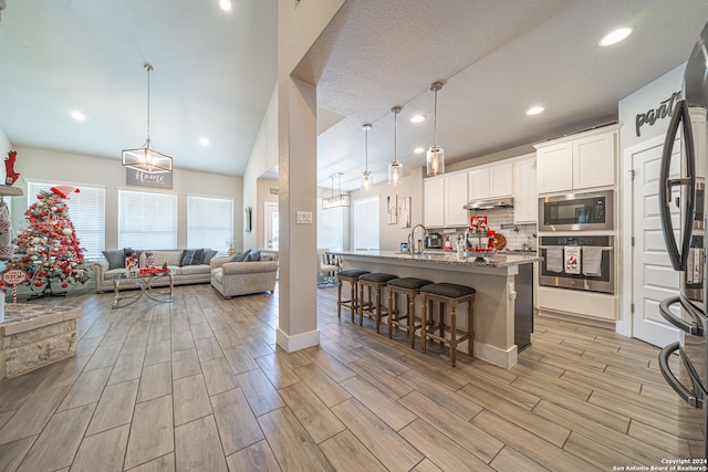 kitchen featuring light stone countertops, appliances with stainless steel finishes, a kitchen breakfast bar, pendant lighting, and white cabinets