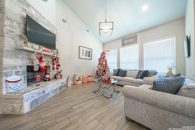 living room with a fireplace, light wood-type flooring, high vaulted ceiling, and an inviting chandelier