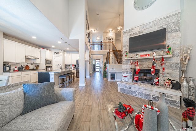 living room with a stone fireplace, sink, a high ceiling, and light wood-type flooring