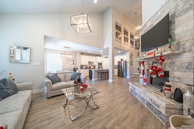 living room with a fireplace, high vaulted ceiling, light hardwood / wood-style floors, and a notable chandelier