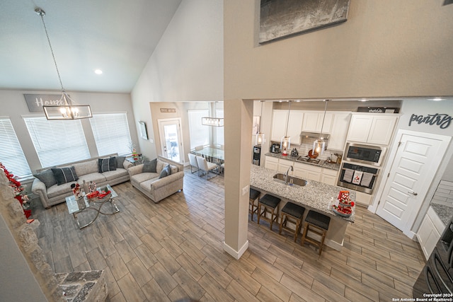 living room featuring a chandelier, wood-type flooring, high vaulted ceiling, and sink