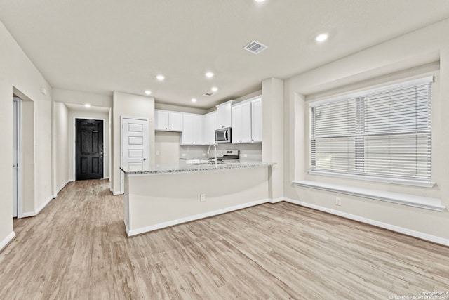 kitchen with appliances with stainless steel finishes, light wood-type flooring, light stone counters, sink, and white cabinetry