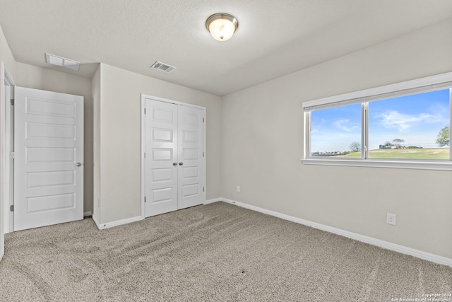 unfurnished bedroom with a textured ceiling, light carpet, and a closet