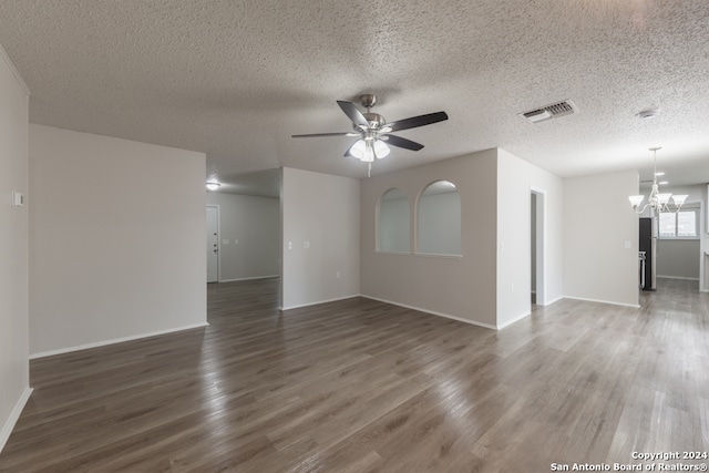 empty room featuring ceiling fan with notable chandelier, a textured ceiling, and dark wood-type flooring