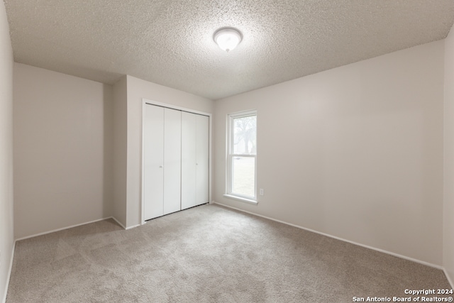 unfurnished bedroom featuring light carpet, a textured ceiling, and a closet