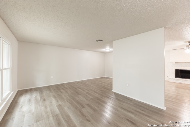 unfurnished room featuring hardwood / wood-style flooring, a textured ceiling, a wealth of natural light, and a brick fireplace