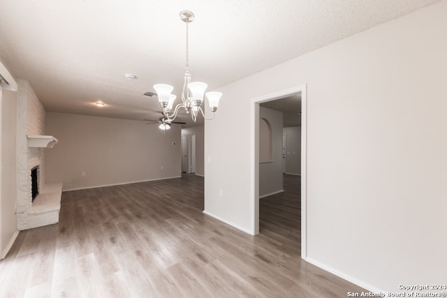 unfurnished living room featuring a textured ceiling, a fireplace, hardwood / wood-style floors, and ceiling fan with notable chandelier