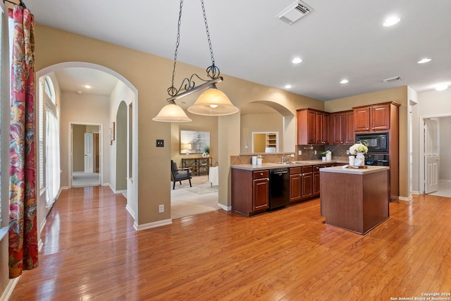 kitchen with light hardwood / wood-style flooring, backsplash, pendant lighting, a kitchen island, and black appliances