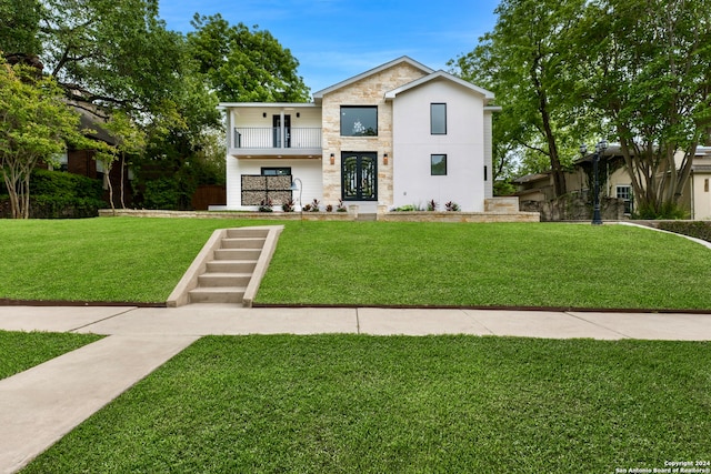 view of front of home with french doors, stone siding, a balcony, and a front lawn