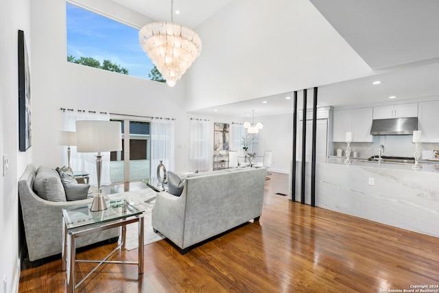 living room with plenty of natural light, wood-type flooring, high vaulted ceiling, and an inviting chandelier