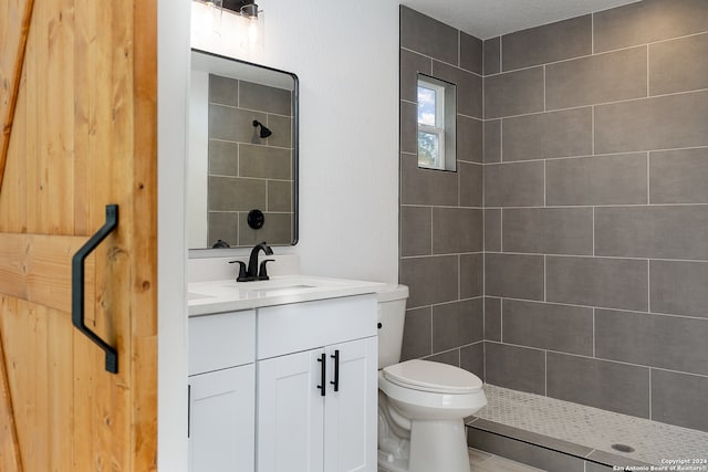 bathroom with a textured ceiling, vanity, toilet, and tiled shower