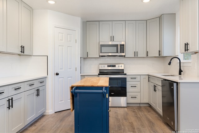 kitchen with wood counters, light wood-type flooring, stainless steel appliances, sink, and a center island