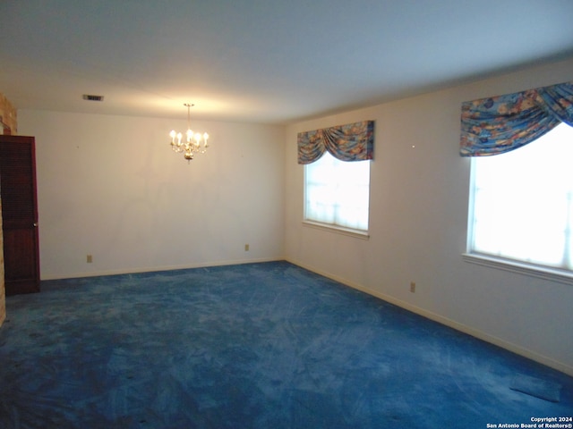 carpeted empty room featuring a notable chandelier and a brick fireplace