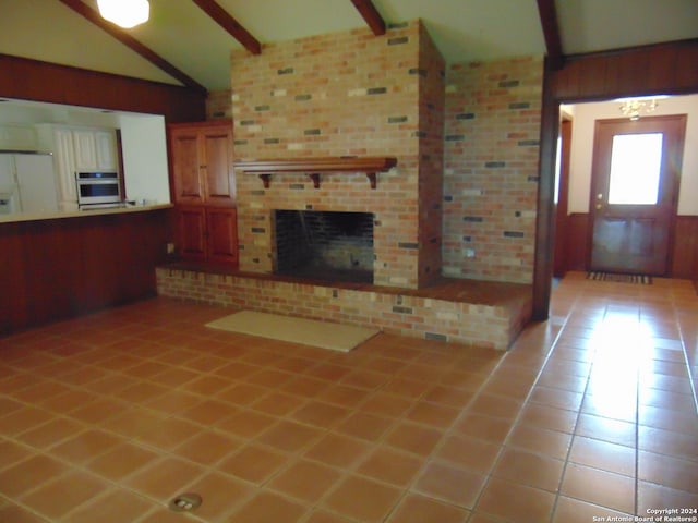 unfurnished living room with light tile patterned floors, vaulted ceiling with beams, a brick fireplace, and wooden walls