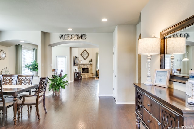 interior space with arched walkways, dark wood-style flooring, recessed lighting, a stone fireplace, and baseboards