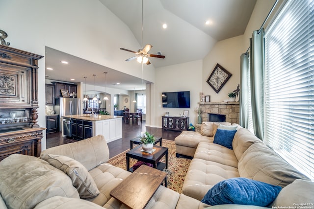 living room featuring ceiling fan, sink, dark wood-type flooring, a stone fireplace, and high vaulted ceiling