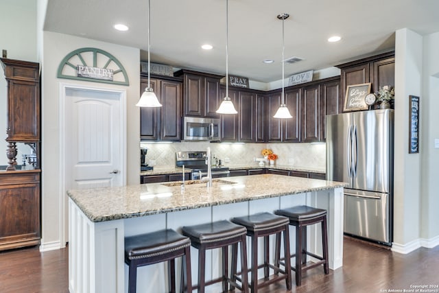 kitchen with dark brown cabinetry, dark hardwood / wood-style flooring, pendant lighting, a center island with sink, and appliances with stainless steel finishes