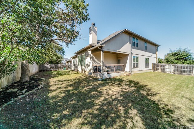 rear view of property featuring a yard, a chimney, a fenced backyard, and stucco siding