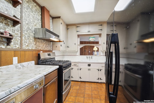 kitchen featuring electric range, white cabinets, wall chimney range hood, and stainless steel gas range