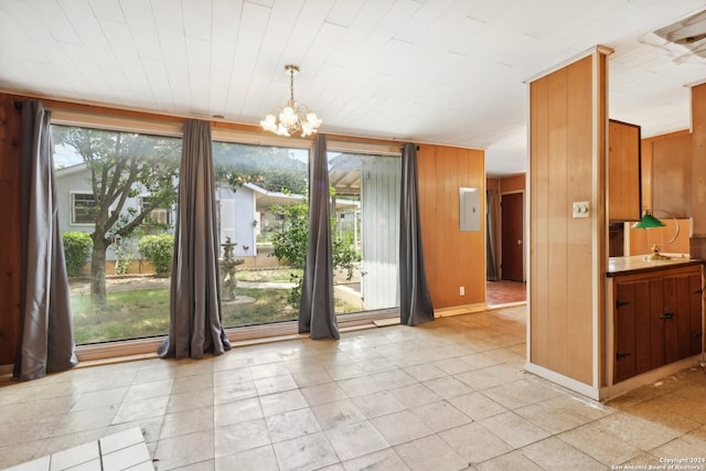 unfurnished dining area featuring a chandelier, light tile patterned floors, electric panel, and wood walls