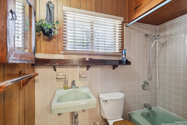 full bathroom featuring tiled shower / bath combo, wood walls, toilet, and sink