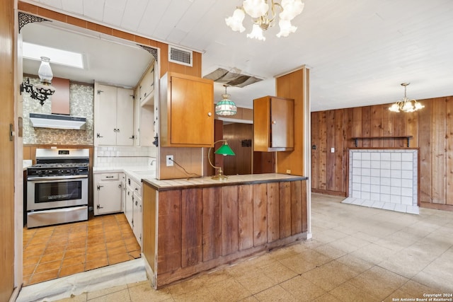 kitchen featuring stainless steel range with gas cooktop, backsplash, a chandelier, decorative light fixtures, and wooden walls