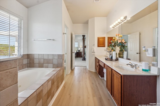 bathroom featuring wood-type flooring, vanity, and tiled tub