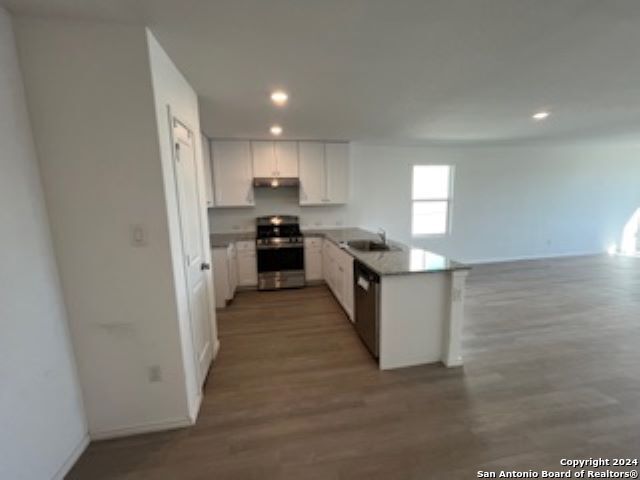 kitchen featuring kitchen peninsula, stainless steel appliances, sink, hardwood / wood-style flooring, and white cabinets