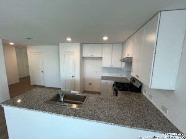 kitchen with white cabinetry, sink, kitchen peninsula, dark stone counters, and range