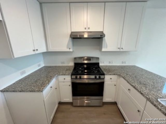 kitchen featuring light stone counters, white cabinetry, and stainless steel stove