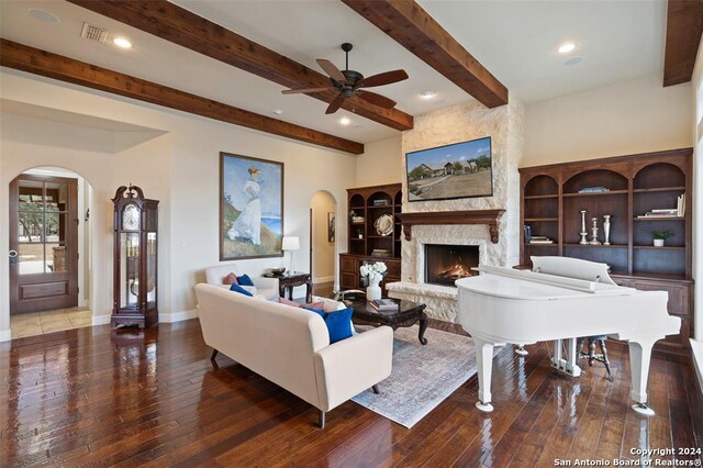 living room with a fireplace, beam ceiling, dark wood-type flooring, and ceiling fan