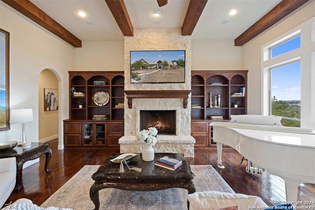 living room featuring beamed ceiling, a stone fireplace, and dark wood-type flooring