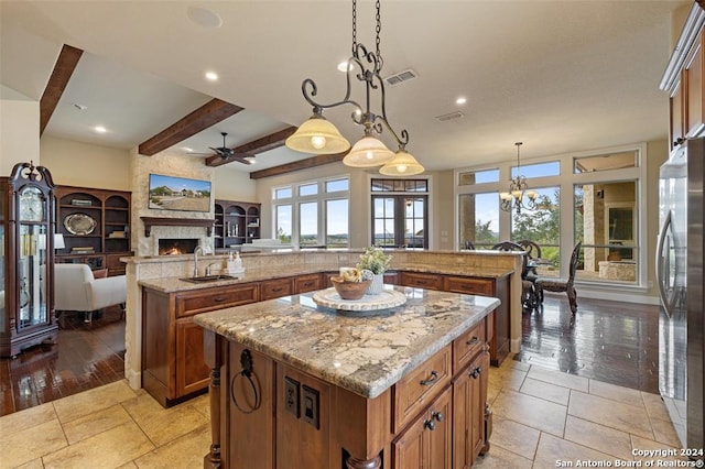 kitchen featuring light wood-type flooring, beam ceiling, decorative light fixtures, stainless steel refrigerator, and a large island