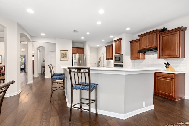 kitchen featuring dark wood-type flooring, a kitchen breakfast bar, backsplash, a center island with sink, and appliances with stainless steel finishes