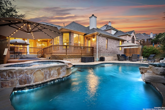 pool at dusk with an in ground hot tub and a deck