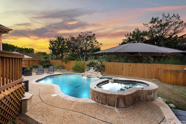 pool at dusk with a patio area and an in ground hot tub