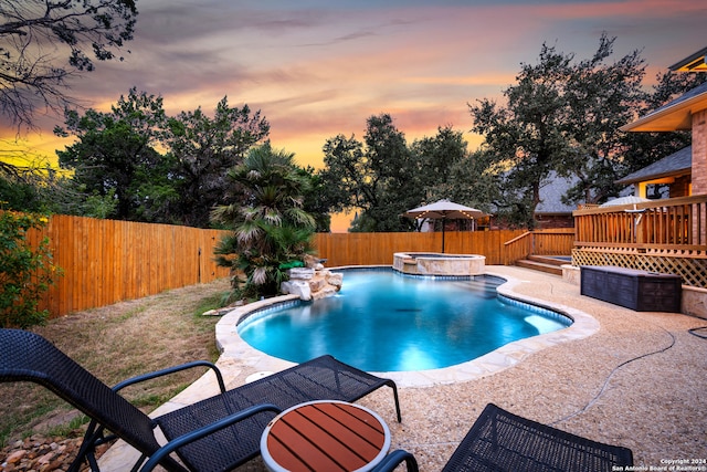 pool at dusk featuring a patio, an in ground hot tub, and a wooden deck