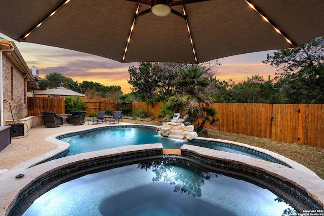 pool at dusk featuring an in ground hot tub and a patio area