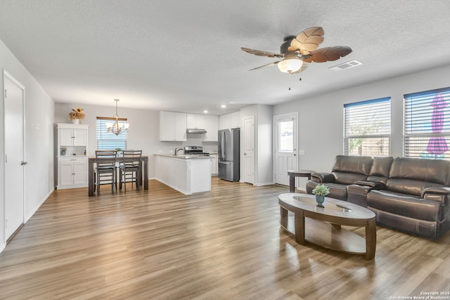 living room with ceiling fan with notable chandelier, a textured ceiling, and light hardwood / wood-style flooring